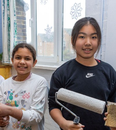 Prep School pupils holding paint brushes to paint a room as part of Make A Difference Day