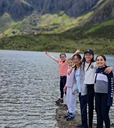 Prep-School pupils enjoying their school trip standing on the shore of a lake with mountains in the background