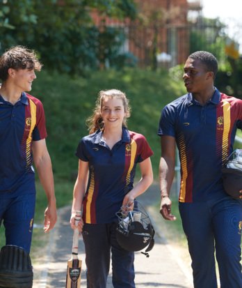 Cricketers in their kit holding cricket equipment walking along the Home Ground