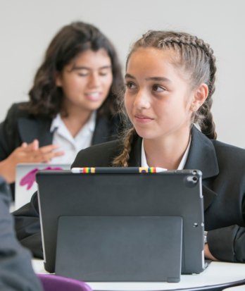 Pupils working on their laptops and listening to their teacher in an English lesson