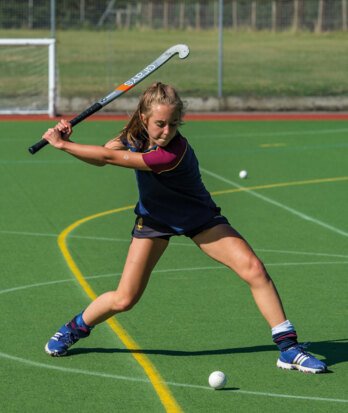 Hockey player raising their stick and looking at the ball ready to strike it towards the goal