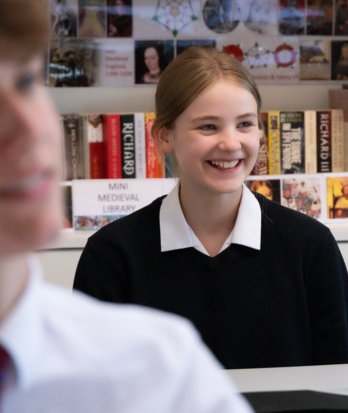 Pupil sitting in the classroom enjoying a History lesson with History books displayed in the background