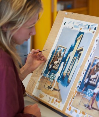 Pupil holding a paint brush comparing her painting to the source photograph