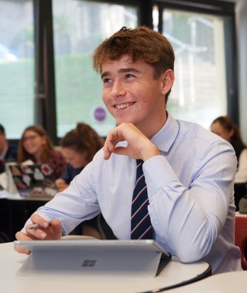 Sixth Form pupil sitting at a desk with their laptop enjoying listening to their teacher in a lesson