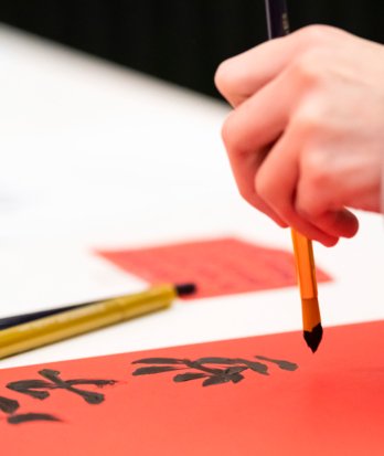 Pupil painting characters onto a red piece of paper in a Mandarin lesson