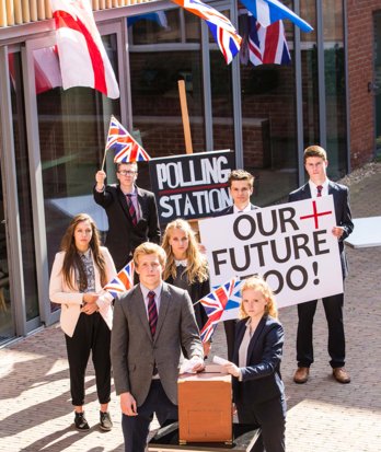 Sixth Form standing outside in the Woolton Quad at the polling station with signs, banners and putting ballots in the box