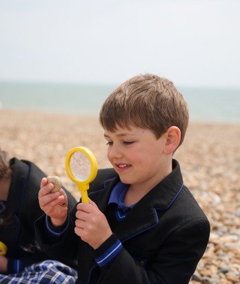 Pre-Prep pupil holding a magnifying glass and examining a stone on the beach