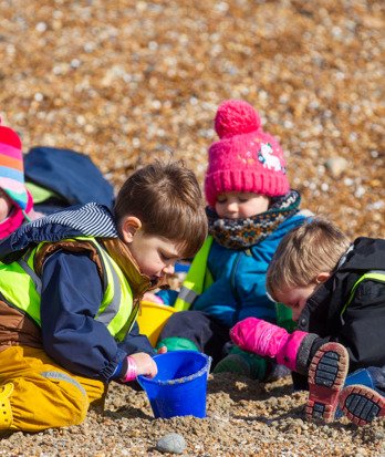 Pre-Prep pupils sitting on the beach examining stones and rocks with buckets and spades on the beach