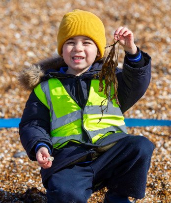 Pre-Prep pupil holding seaweed and sitting on the beach at Beach School