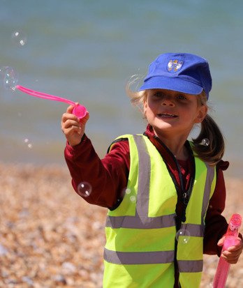 Pre-Prep pupil in a high-vis jacket blowing bubbles on the beach at Beach School