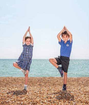 Pre-Prep pupils standing on one leg practicing yoga on the beach on a sunny day