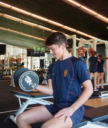 Pupil in the Blackshaw Gym doing a bicep curl with Brighton College Sport branded dumbbells