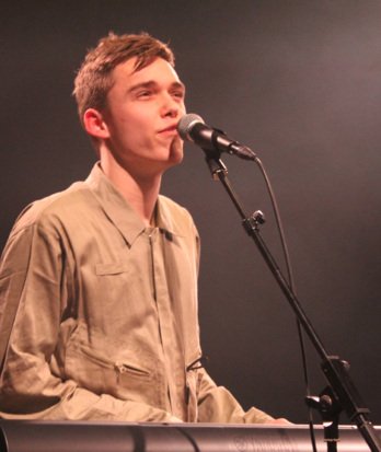 Old Brightonian Stan singing and playing the piano on stage in a concert