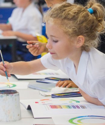 Prep School pupil dipping their paintbrush into water and painting the colour wheel in an Art lesson