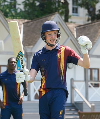 Pupil in 1st XI team cricket kit and batting kit enjoying playing in front of the Sammy Woods Pavilion in a Games session