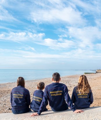 Pupils sitting on the beach in their sports kit on a sunny day