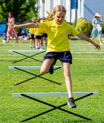 Pre-prep pupil in St David's House jumping over hurdles in a Sports Day Race on the field