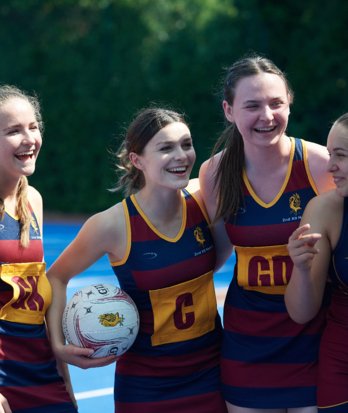 Pupils in netball dresses and holding a ball laughing together on the court