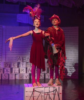 Prep School pupils standing on blocks with a megaphone on stage in costume performing in Matilda