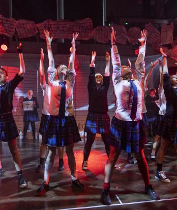 Prep School pupils performing on stage in the Great Hall a song from their production of Matilda in school uniform