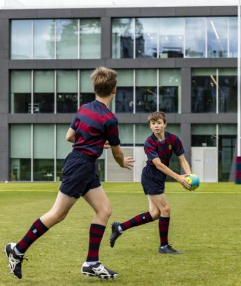 Pupils in rugby kit passing a ball on the Home Ground in a games session