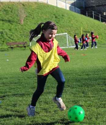 Pre-Prep pupil dribbling a football on the field in a Games lesson