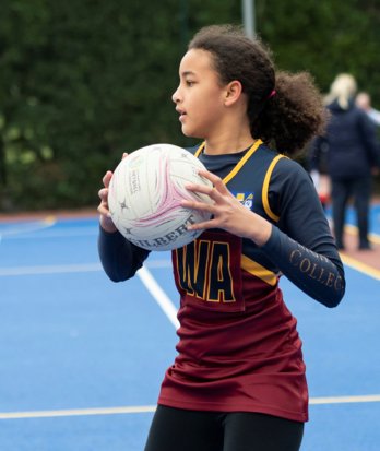 Prep School pupil holding the ball on the court playing in a Netball match against another school