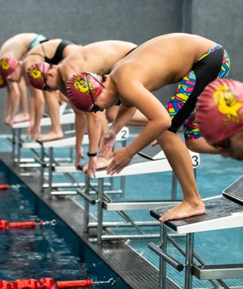 Swimmers on the blocks preparing to dive into the pool in the SSS