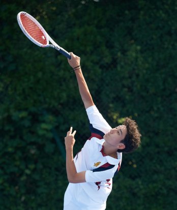 Pupil in tennis whites holding their racket in the air as they serve the ball