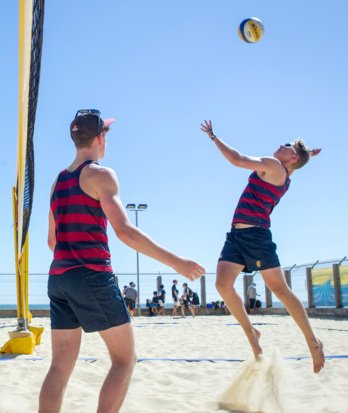 Pupil jumping up to spike a ball by the net at a Volleyball match at Yellowave