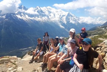  Pupils at the top of a hill having completed a hike with a beautiful view of mountains in the background 