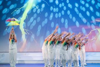  Prep School pupils in white trousers and rainbow tops performing a group dance on stage 