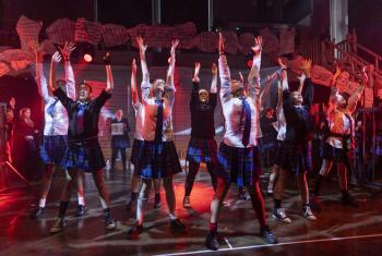  Prep School pupils performing on stage in the Great Hall a song from their production of Matilda in school uniform 