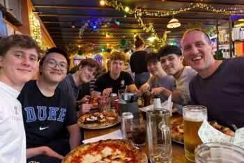  Tutor group at a restaurant eating pizza together with their tutor 