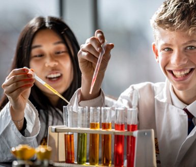  Pupils putting different coloured substances into test tubes with pipettes as part of a science experiment 