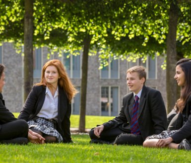  Pupils sitting on the grass in a group talking to each other in the Quad 