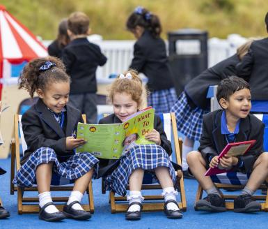  Pre-Prep pupils sitting in the playground and reading a book together at break time 