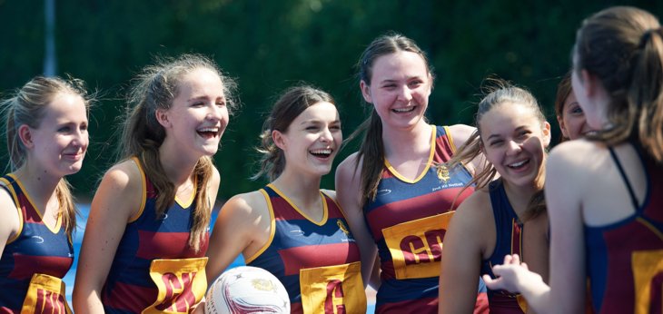  Pupils in netball dresses with a ball standing on the court together 