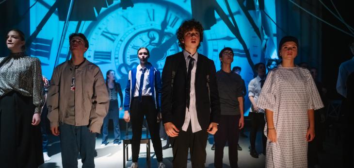  Middle School pupils on stage performing in A Monster Calls with a projection of a clock on the wall 