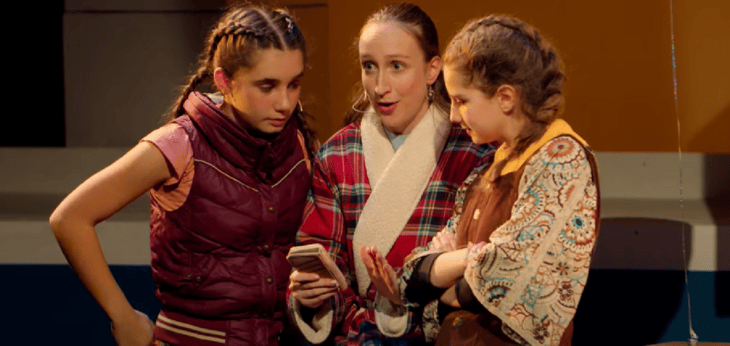  Alice in a dressing gown holding a phone on stage in a play with her theatre group 