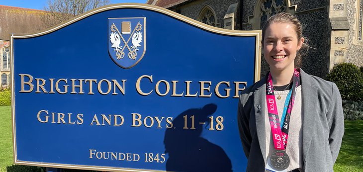  Olivia Haverson standing in front of the Brighton College sign with her Brighton Marathon medal 