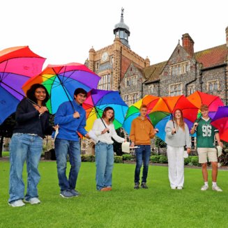 Pupils in the Quad celebrating their results on GCSE Results Day standing under rainbow umbrellas