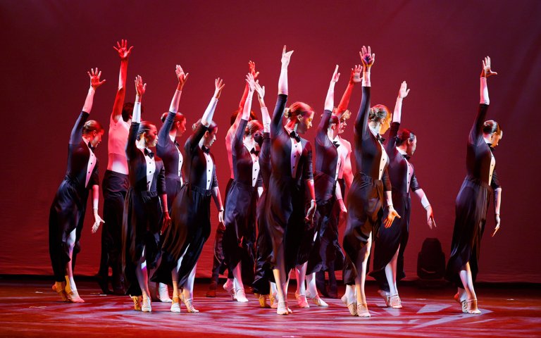  Group on stage performing a piece in a black-tie inspired costume in the Dance Show 