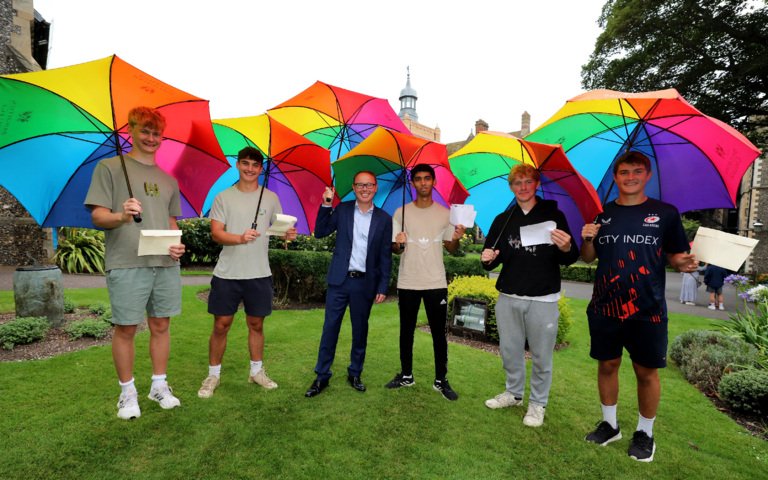  Pupils in the Quad celebrating their results on GCSE Results Day standing under rainbow umbrellas with Richard Cairns 