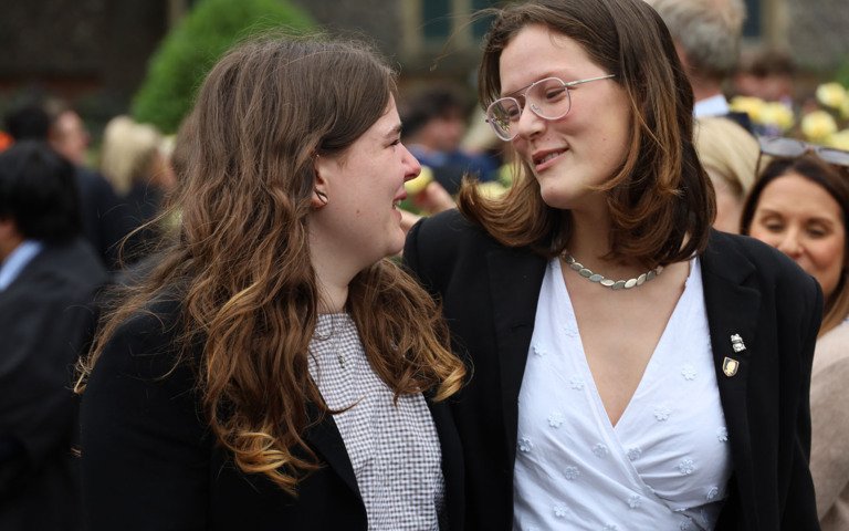  Pupils with their arms around each other and smiling as they walk out of their Chapel after Graduation 