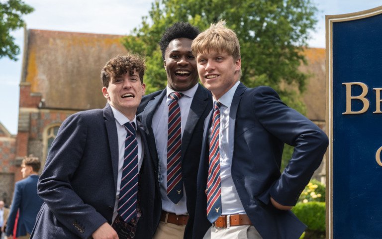  Pupils with their arms around each other smiling by the Brighton College sign after their Graduation 