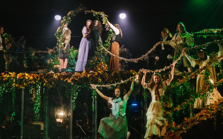  Pupils on the floral set of the production of Into the Woods holding up garlands 