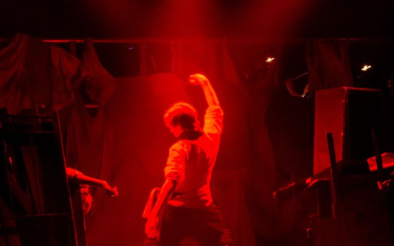  Pupil in red light with their fist in the air in the barricade scene in Les Misérables production 