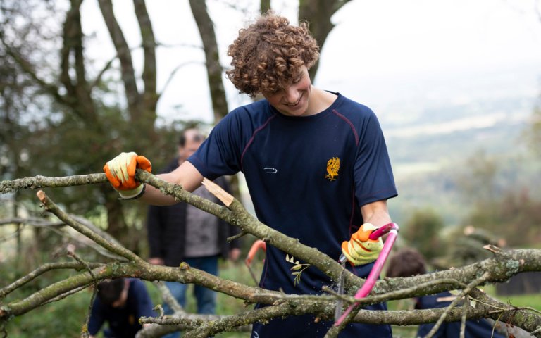  Pupil with a saw and gardening gloves cutting off branches volunteering as part of Make A Difference Day 