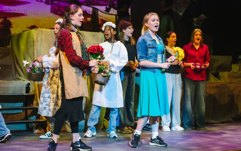  Pupils on stage holding flowers singing a musical number during a performance of Oliver 